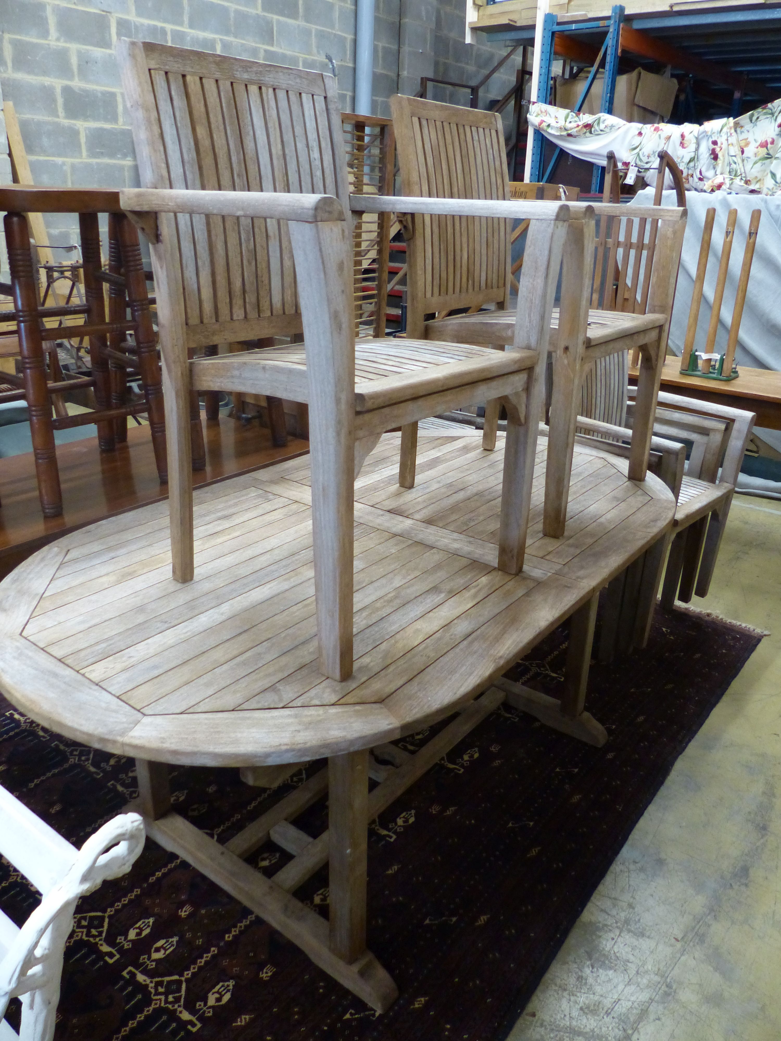 An oval weathered teak extending garden table, 240cm extended, width 100cm, height 74cm and eight stacking elbow chairs